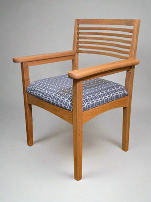Wooden chair with a patterned cushion against a neutral wall.