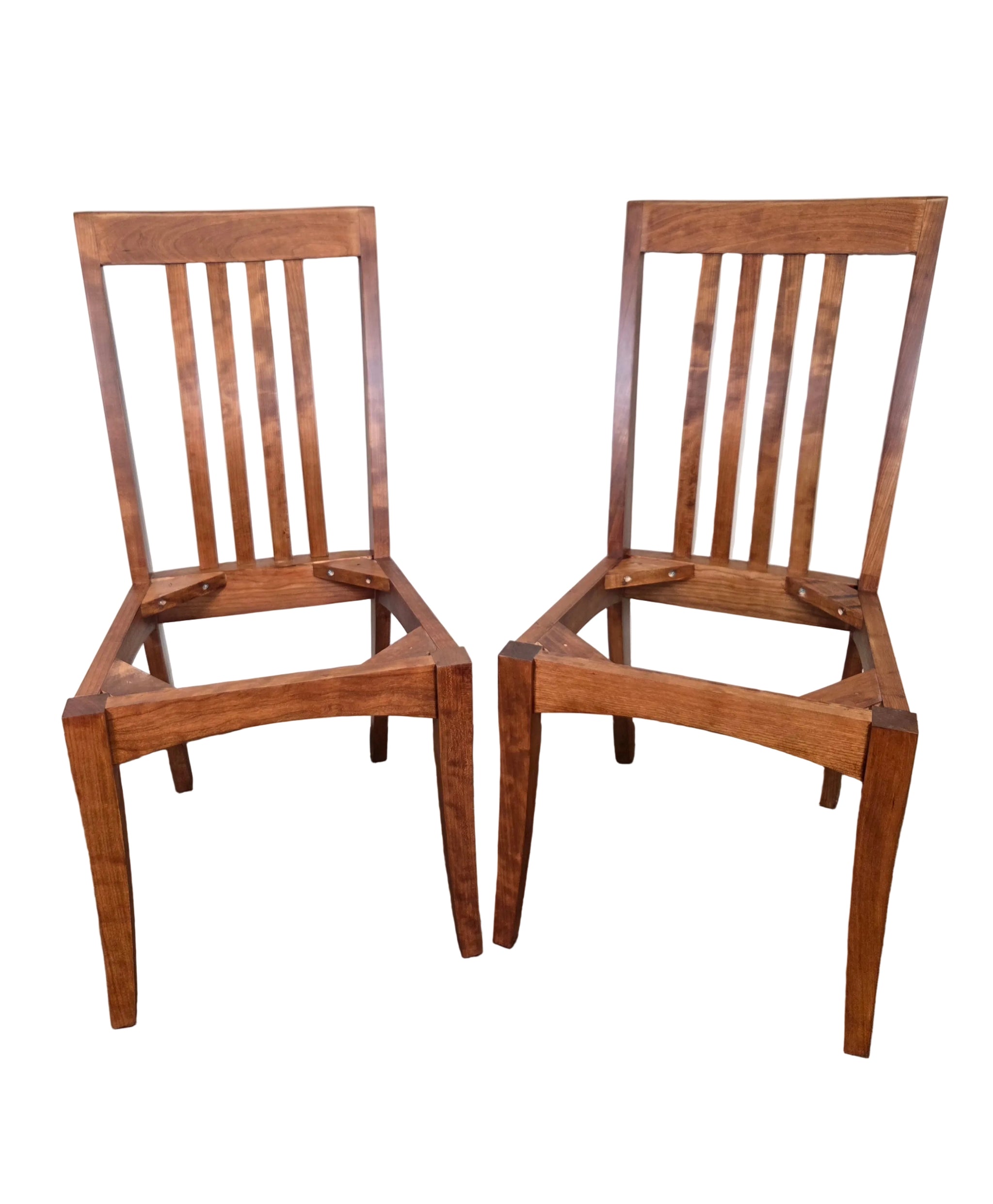 Two wooden chairs on a carpeted floor with a white wall background
